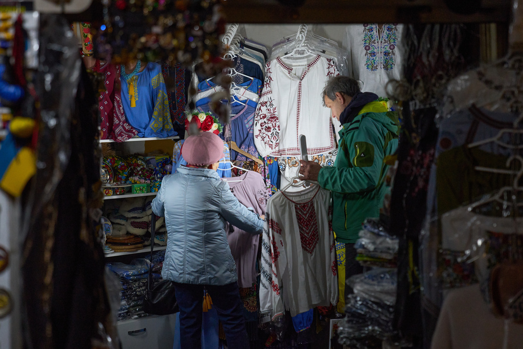 A vendor shines a torch on the clothes for a customer in a small private shop during blackout caused by Russia's air attacks on the country's energy sector in central Kyiv, Ukraine. Source: AP