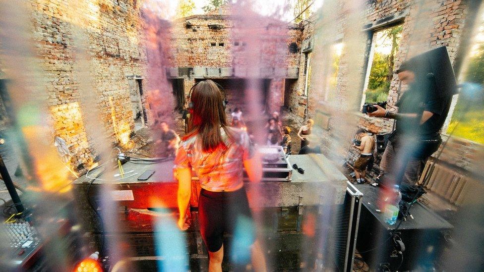A DJ performs at an open-air rave inside the ruins of a bombed-out building near Kyiv, Ukraine, July 2022. Young people gather in abandoned industrial sites and war-damaged spaces to dance, volunteer, and raise funds for reconstruction, keeping Ukraine’s rave culture alive despite the ongoing Russian invasion. Source: BBC Photo, via Newsbeat